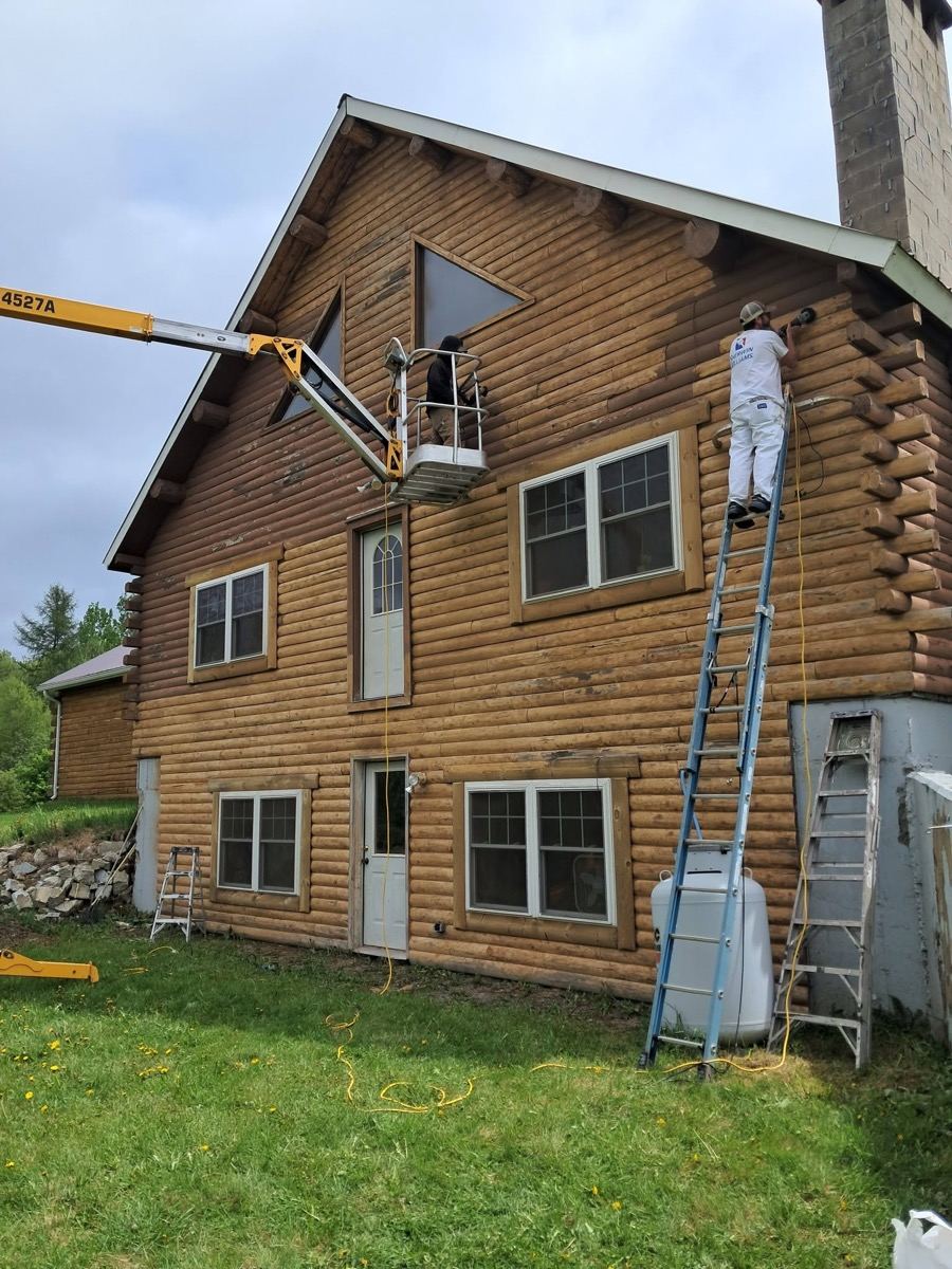 Faded log home mid-restain with the Freedom Painting crew on a lift